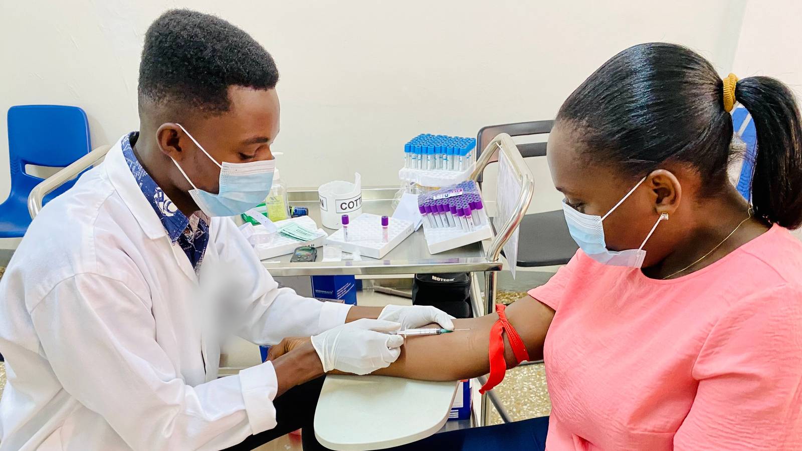 A healthcare worker in a lab coat drawing blood from a woman's arm