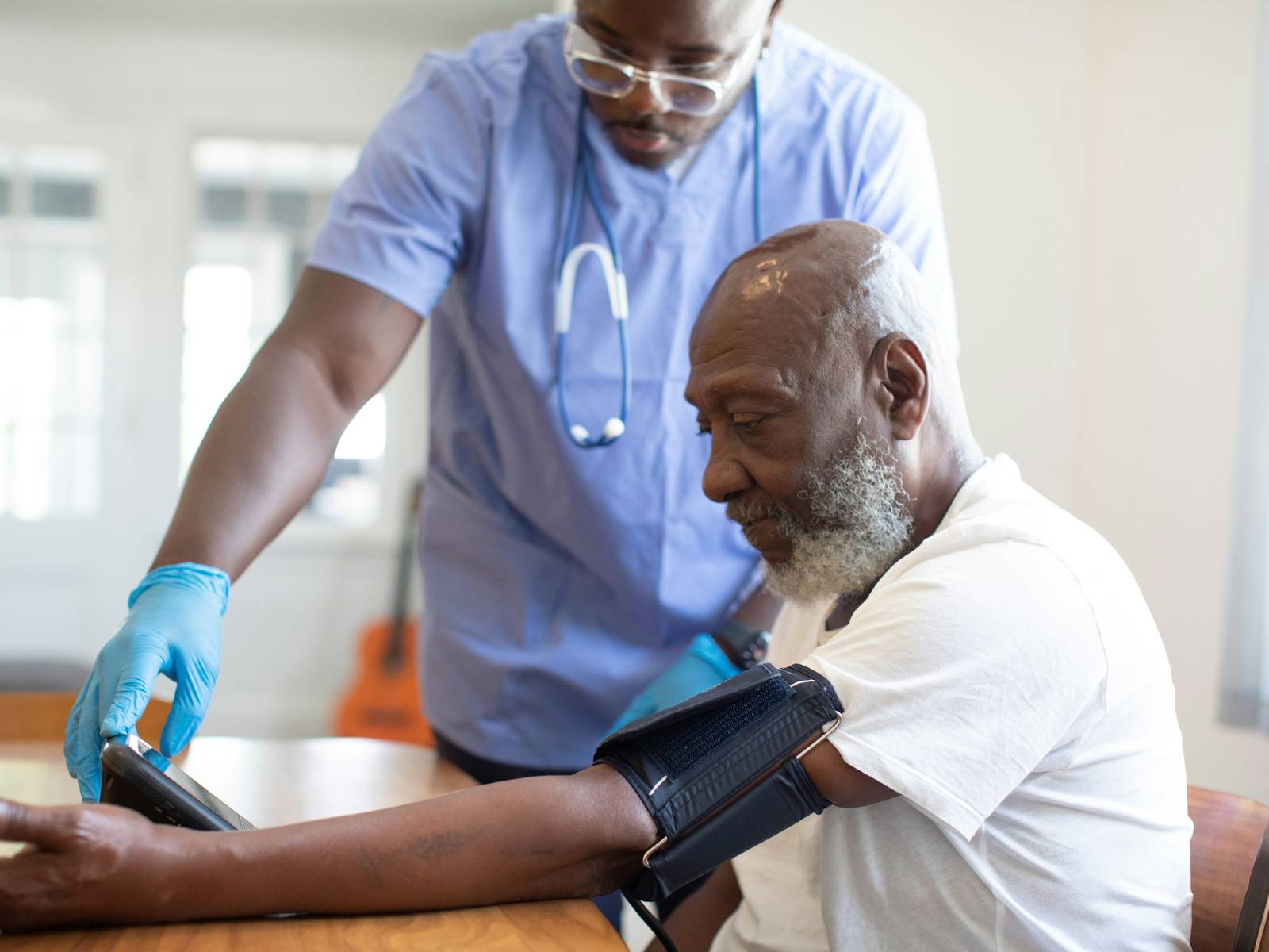 A healthcare worker in scrubs taking an older man's blood pressure at a table