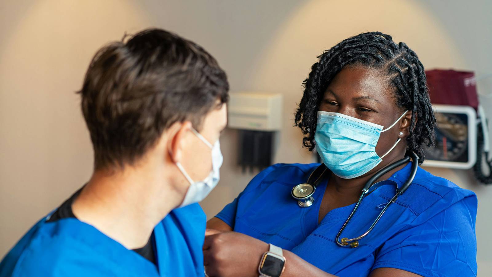 A healthcare worker in blue scrubs and a face mask holding a person's arm